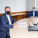 Zwei maskierte Personen unterschreiben ein Dokument