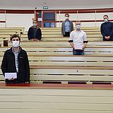 Personen mit Masken stehen in einem Hörsaal