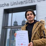 Eine Person mit einem Steiger-College-Zertifikat vor dem Eingang zum Hauptgebäude der TU Clausthal