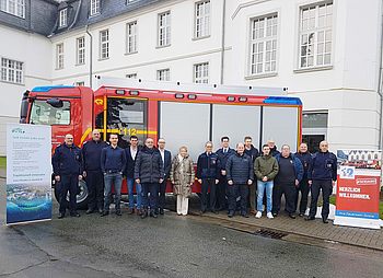 Menschen stehen in einer Reihe vor einem Feuerwehrauto. 