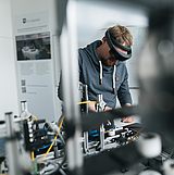 Person mit Brille arbeitet an einer Maschine 